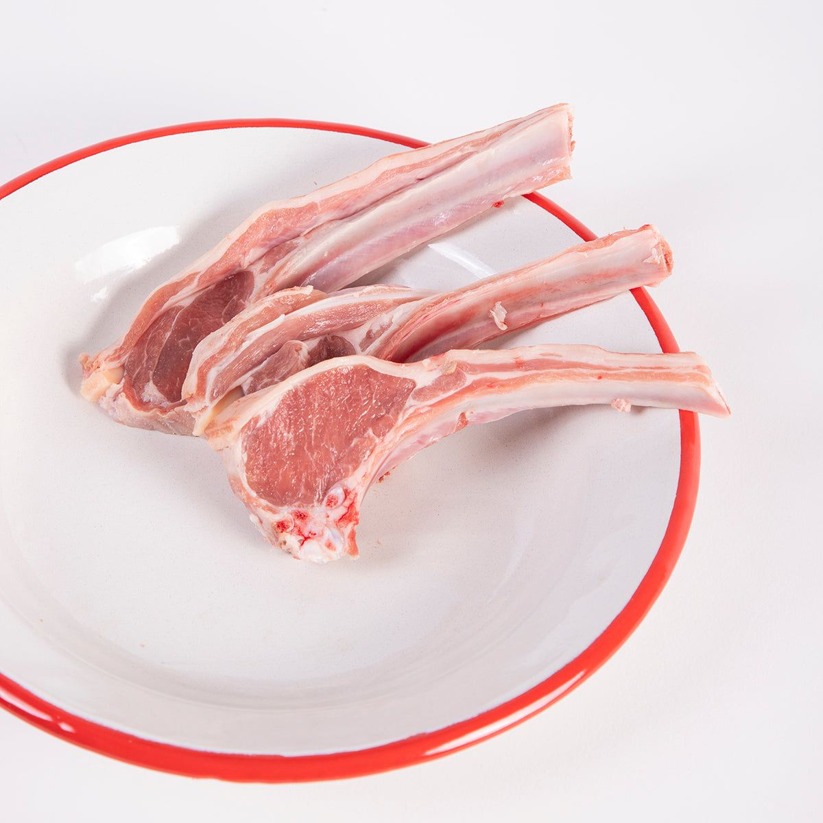 plato blanco con filo rojo y tres chuletas frescas de cordero recental